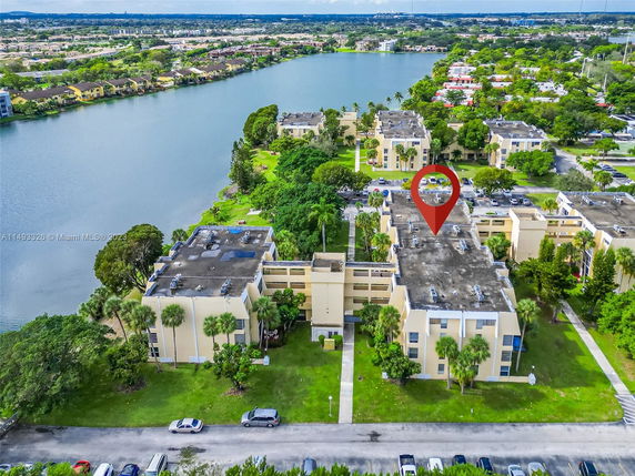 Aerial view of residential buildings near a lake with surrounding greenery and roads.
