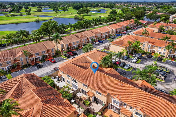 Aerial view of residential neighborhood with red-tiled roofs and surrounding greenery and water features.