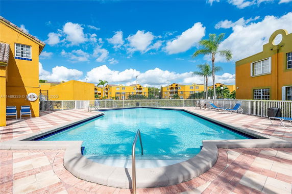 Outdoor swimming pool surrounded by a fence with buildings in the background.