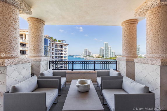 Panoramic view from a balcony with modern sofas overlooking a waterfront and city skyline.