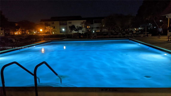 Night view of an outdoor swimming pool with buildings in the background.