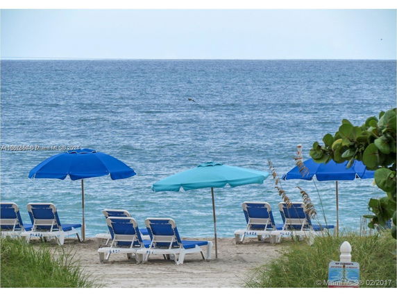 Beach scene with blue and turquoise umbrellas and lounge chairs facing the ocean.