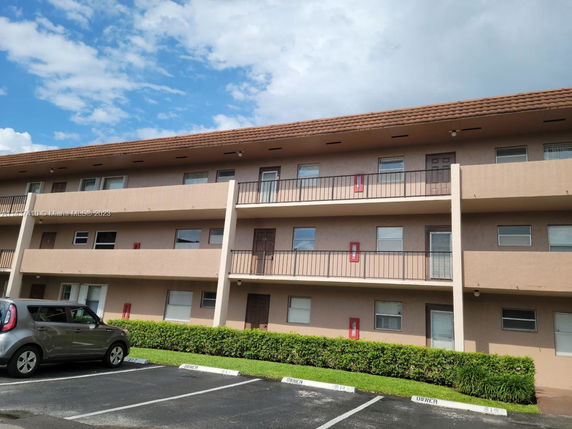 Front view of a three-story residential building with balconies and a parking area in front.