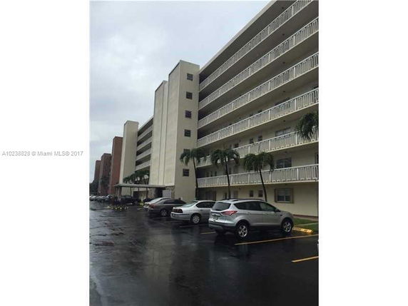 Front view of a multi-story apartment building with a parking area and balconies.