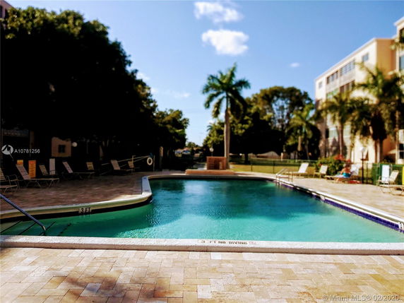 View of a swimming pool surrounded by lounge chairs with a building in the background.