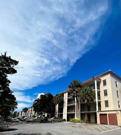 Front view of a multi-story apartment building with balconies and adjacent parking area.