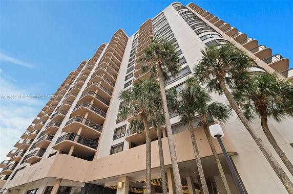 Elevated view of a tall multi-story building with balconies and palm trees at the base.