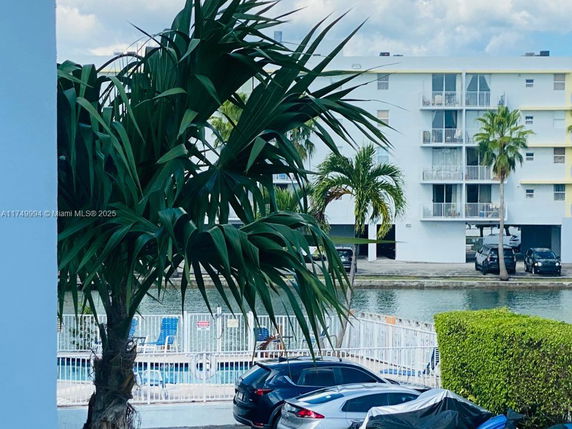 View of a multi-story building with balconies, surrounded by palm trees and cars parked in front.