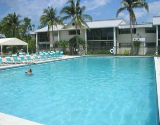 Outdoor swimming pool in front of a two-story building with palm trees around.