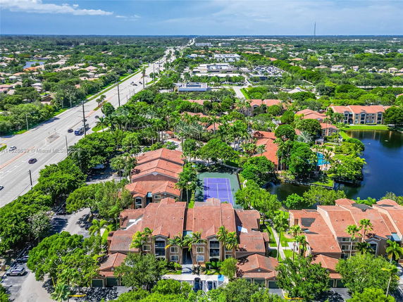 Aerial view of a residential area with townhouses, tennis court, and surrounding greenery.