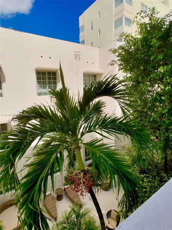 Exterior view of a white building with large windows and surrounding palm trees.
