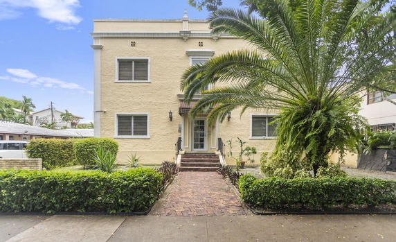 Front view of a two-story house with large windows and a palm tree in the yard.