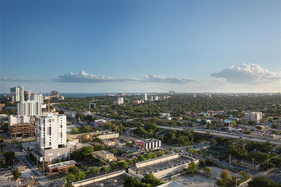 Panoramic view of a cityscape with tall buildings and a lush green landscape extending towards the horizon.