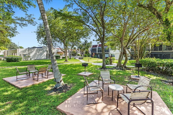 View of outdoor seating area with chairs and tables, surrounded by trees and buildings.