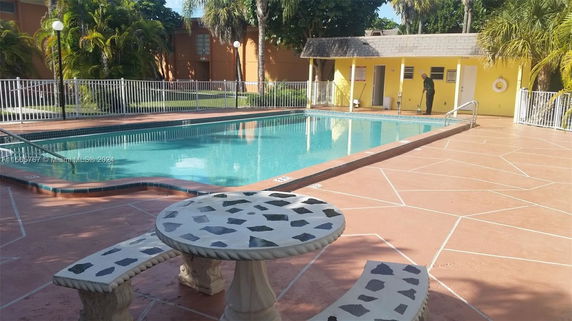 Outdoor swimming pool with a surrounding fence and a small building nearby.