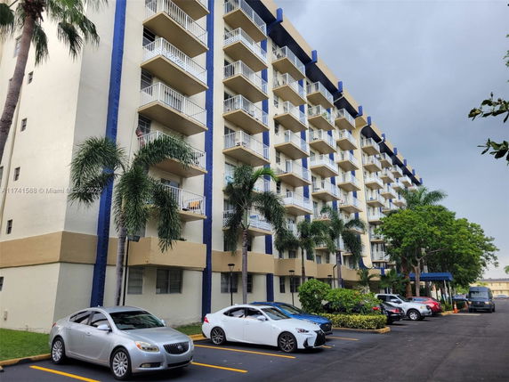 Front view of a multi-story apartment building with balconies and parking area in front.