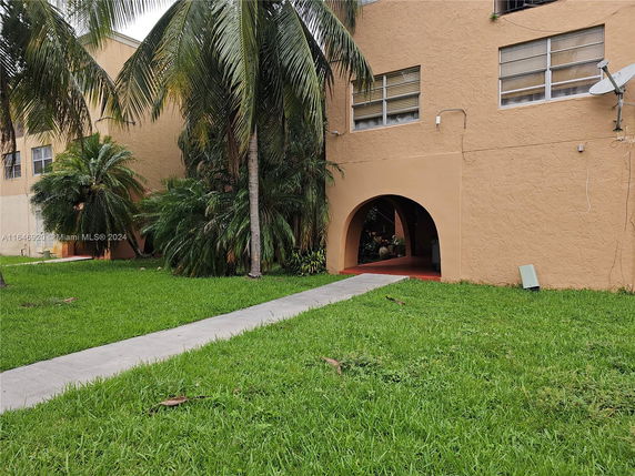 Front view of a building with arched entrance and windows, surrounded by palm trees.