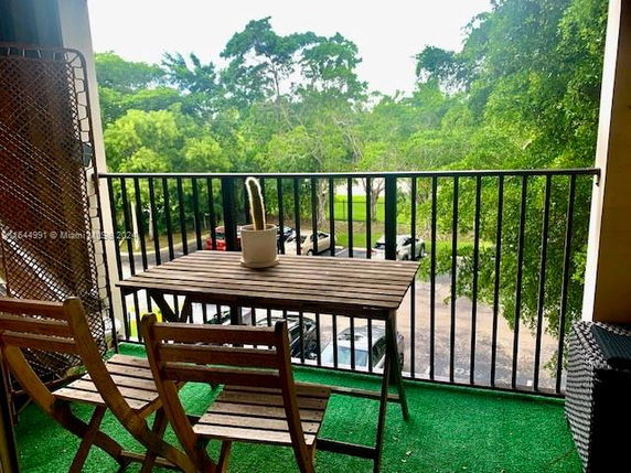 View from a balcony with a wooden table and chairs, overlooking trees and parked cars.