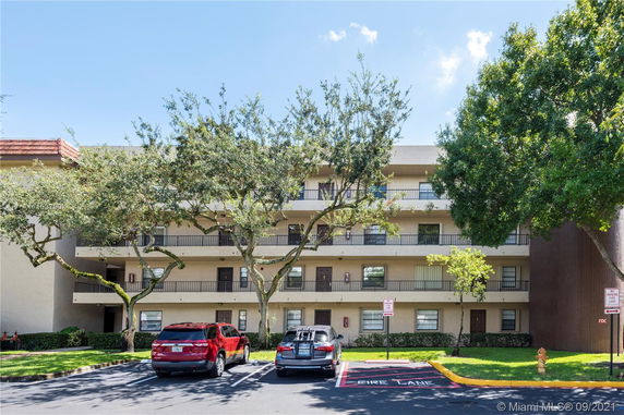 Front view of a multi-story building with balconies and parked cars.