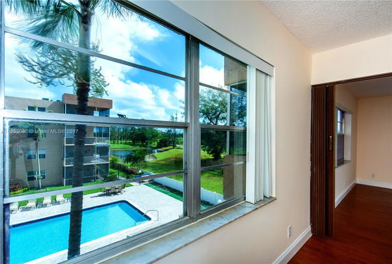 View from a window showing an outdoor swimming pool and surrounding greenery.