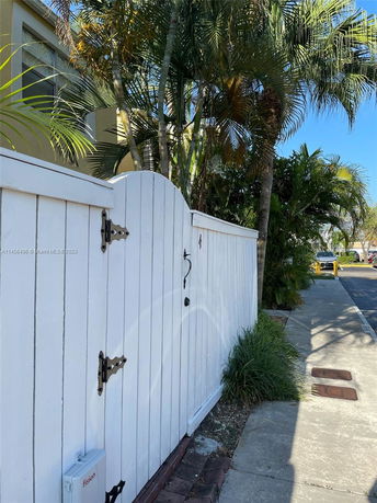 Front view of a house with a white wooden gate and palm trees.