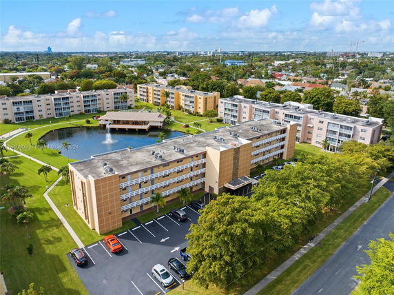 Aerial view of a residential complex with multiple mid-rise buildings and a pond with a fountain.