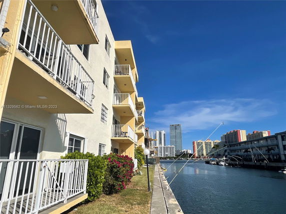 Side view of a multi-story building with balconies overlooking a canal and neighboring high-rise structures.