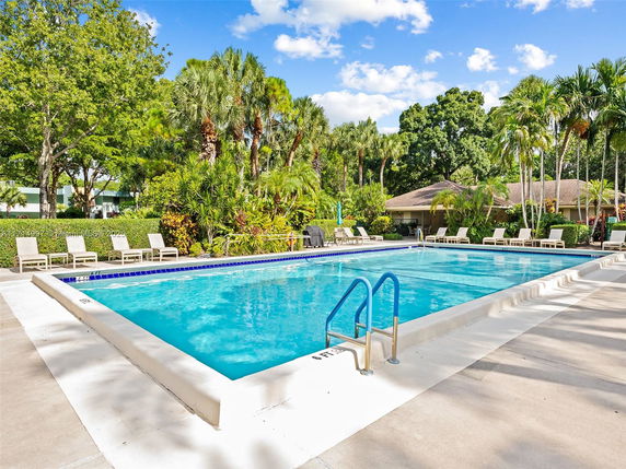 Outdoor swimming pool surrounded by lounge chairs and tropical vegetation.