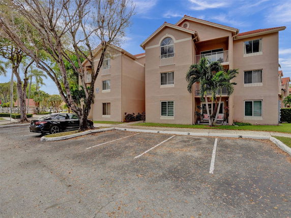 Front view of a three-story residential building with adjacent parking area.