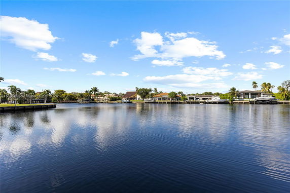 View across a body of water with houses and boats along the shoreline under a blue sky with clouds.