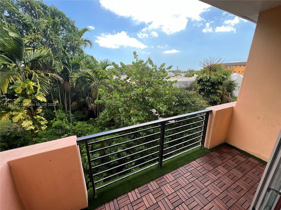 Outdoor balcony with railing overlooking green vegetation and nearby buildings.