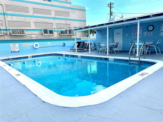 Outdoor swimming pool area with surrounding lounge chairs and a building in the background.