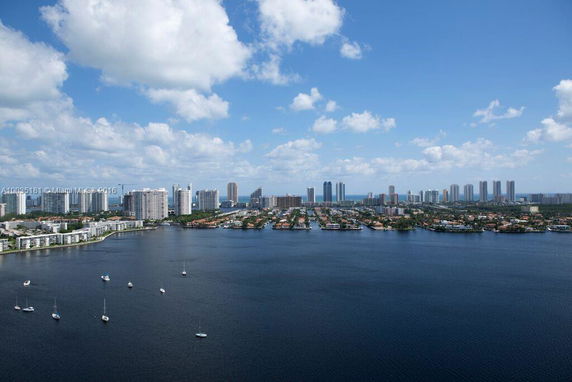 Panoramic view of a city skyline with numerous high-rise buildings along a waterfront, under a clear blue sky.
