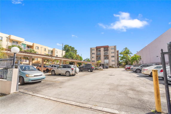 Outdoor parking area with several cars and a view of multi-story residential buildings.