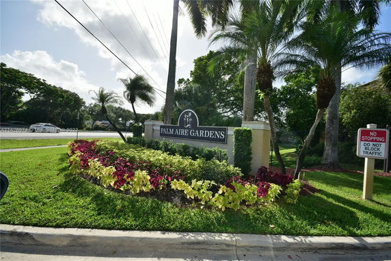 Signage for Palm Aire Gardens with landscaped plants and palm trees.