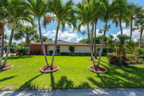 Front view of a single-story house with a manicured lawn and palm trees.