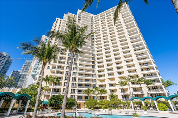 Front view of a multistory building with balconies and palm trees.