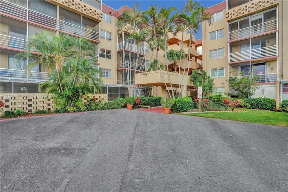 Front view of a multi-story residential building with balconies and tropical landscaping.
