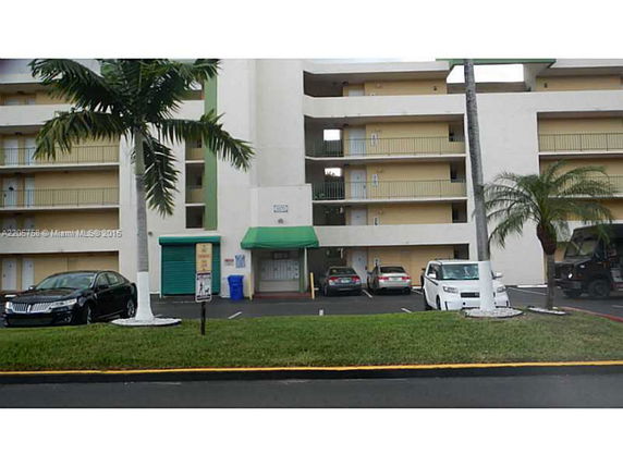 Front view of a multi-story apartment building with parking spaces and a green awning above the entrance.