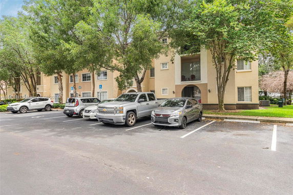 Parking area with several vehicles in front of a multi-story residential building.