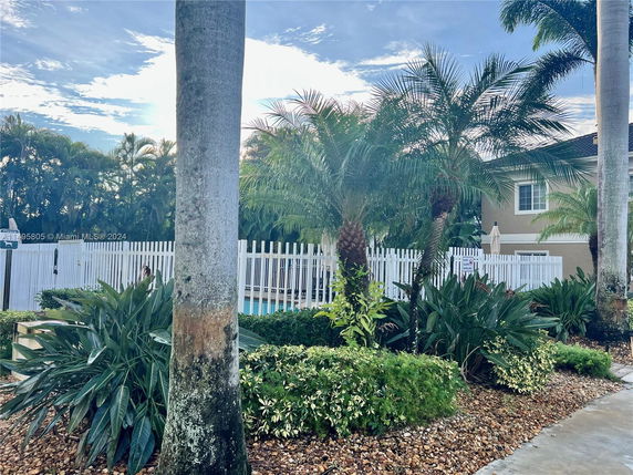 View of outdoor area with palm trees and a white fence around a pool.