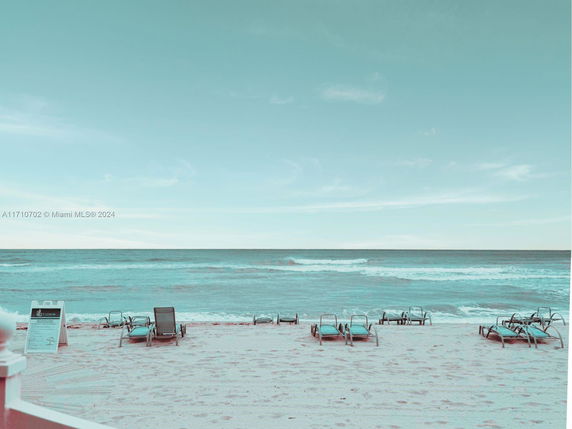View of a sandy beach with several lounge chairs facing the ocean.