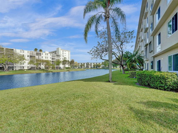 View of residential buildings near a water body with grassy areas and trees.