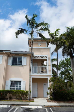 Front view of a two-story building with a balcony and palm trees.