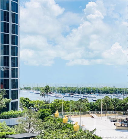 View from a building overlooking a marina with several boats, surrounded by greenery and buildings.