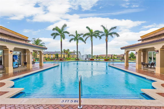 Outdoor swimming pool area with palm trees and surrounding buildings.
