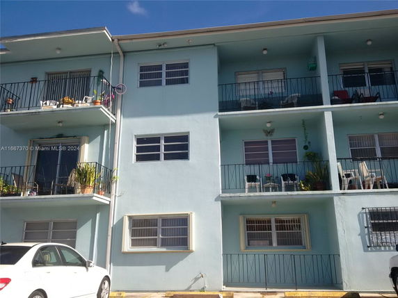 Front view of a three-story apartment building with balconies and a parking area in front.
