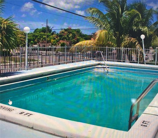Outdoor swimming pool with surrounding fence and palm trees.