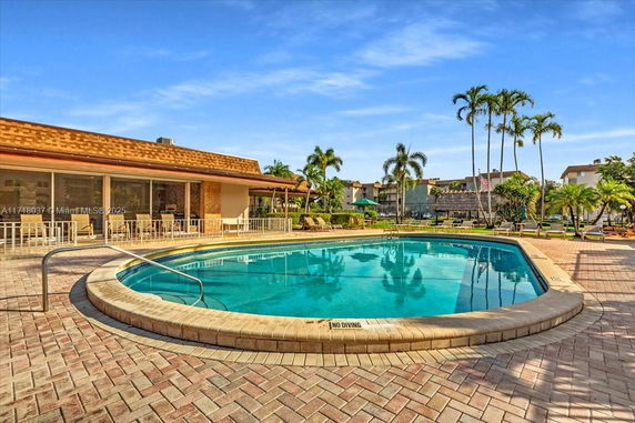 Outdoor area with a swimming pool surrounded by paved patio and building structure.