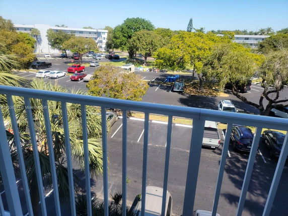 View from a building showing a parking area with multiple cars and trees in the surroundings.